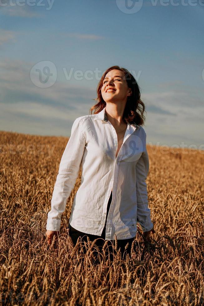 gelukkige jonge vrouw in een wit overhemd in een tarweveld. zonnige dag. foto