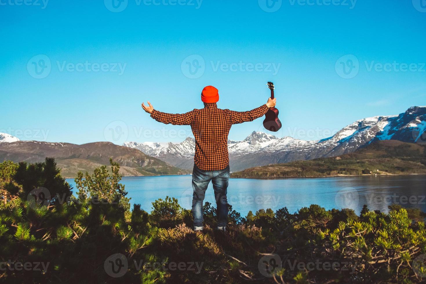 man met een gitaar op de achtergrond van bergen, bossen en meer foto