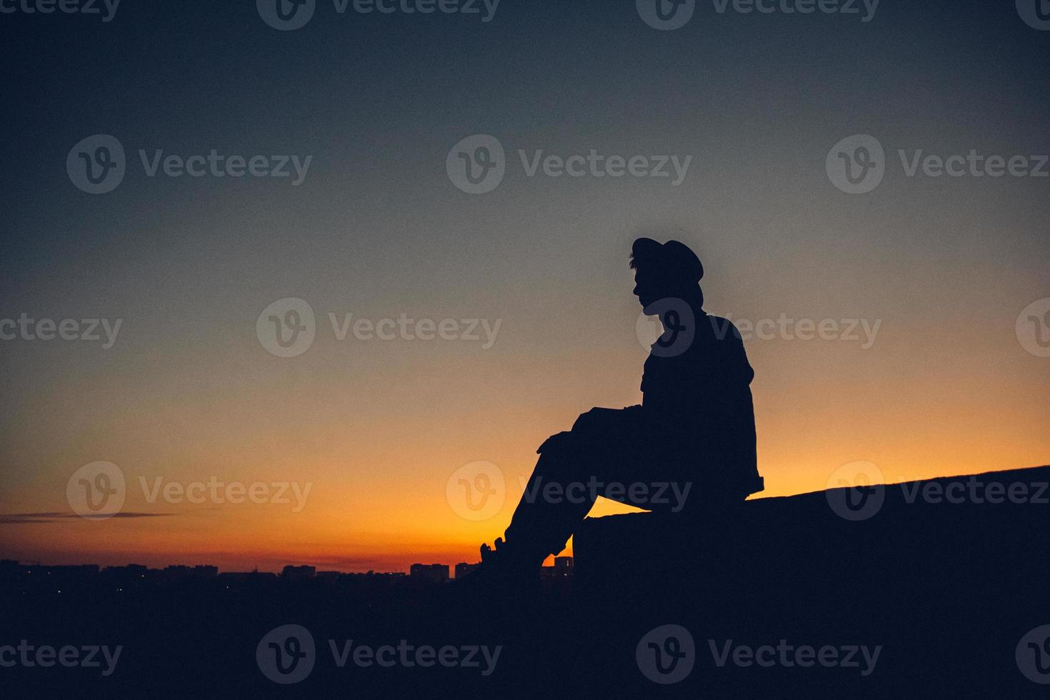 silhouet van het portret van een man met hoed die naar de zonsondergang over de stad kijkt foto