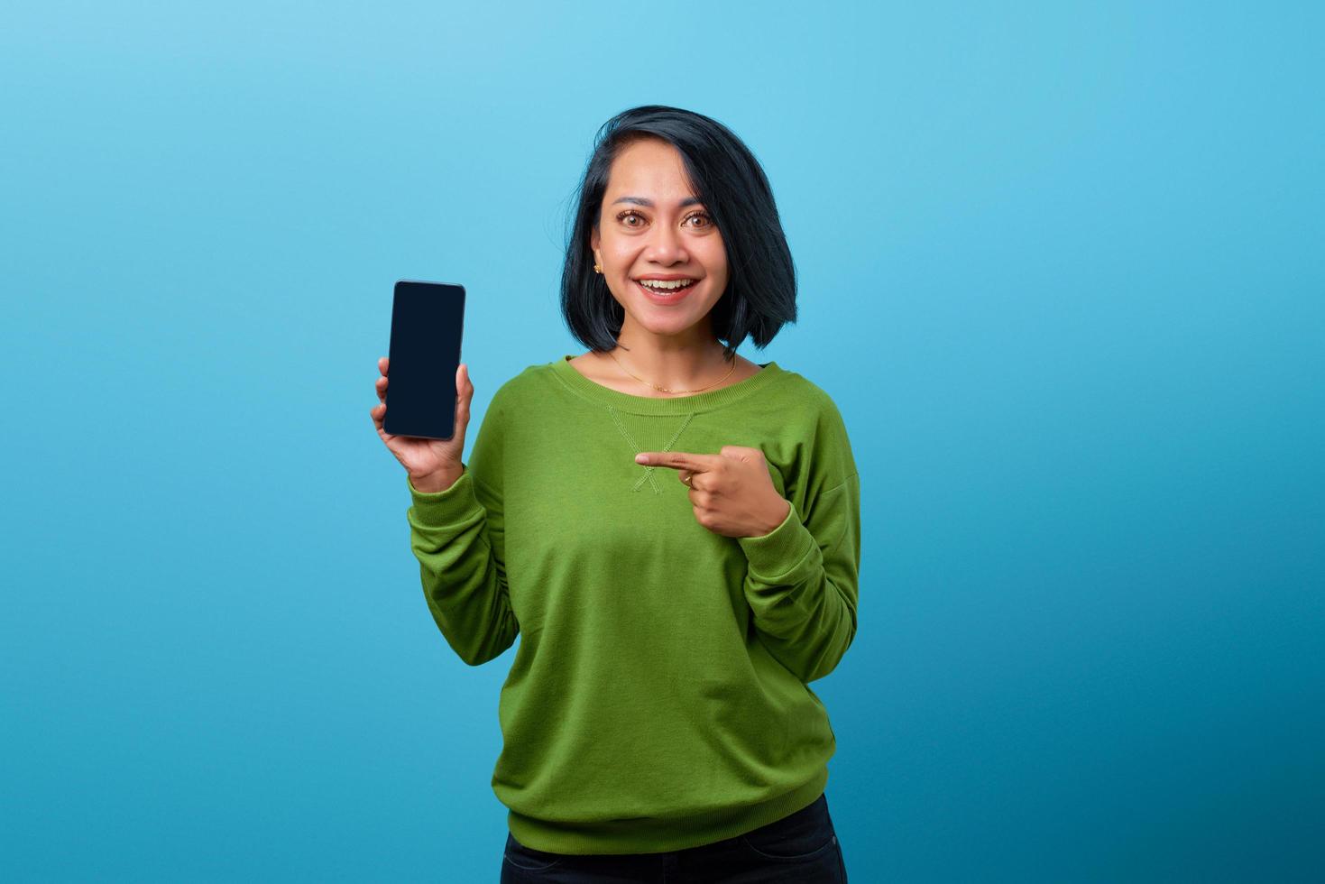 Aziatische vrouw die het lege smartphonescherm over blauwe achtergrond toont foto