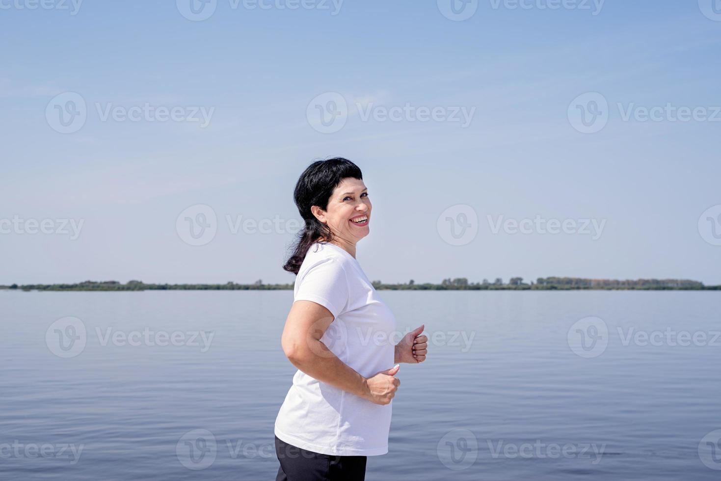 actieve lachende senior vrouw joggen in de buurt van de rivier foto