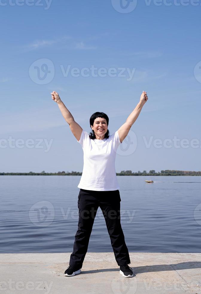 actieve en gelukkige senior vrouw die aan het trainen is in de buurt van de rivier foto