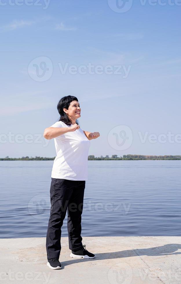 actieve en gelukkige senior vrouw die aan het trainen is in de buurt van de rivier foto