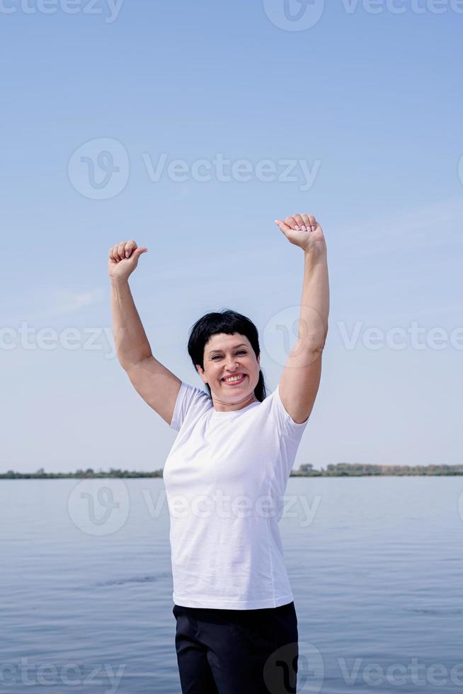 actieve vrouw die aan het oefenen is in de buurt van de rivier, staand met de armen omhoog foto