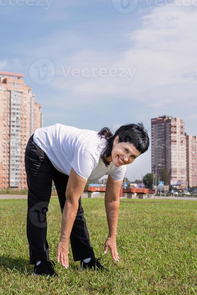 Glimlachende senior vrouw die zich buiten in het park aan het opwarmen is foto