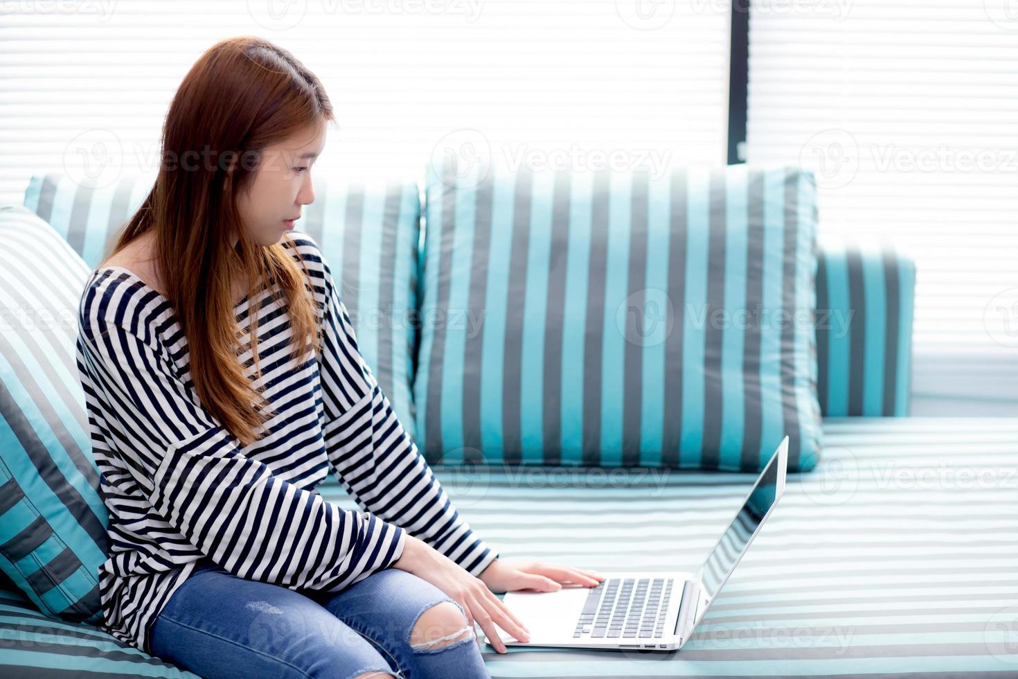 mooi van portret jonge aziatische vrouw die laptop gebruikt voor vrije tijd op de bank in de woonkamer, meisje dat online werkt met een notebook freelance met een gelukkig, communicatief bedrijfsconcept. foto