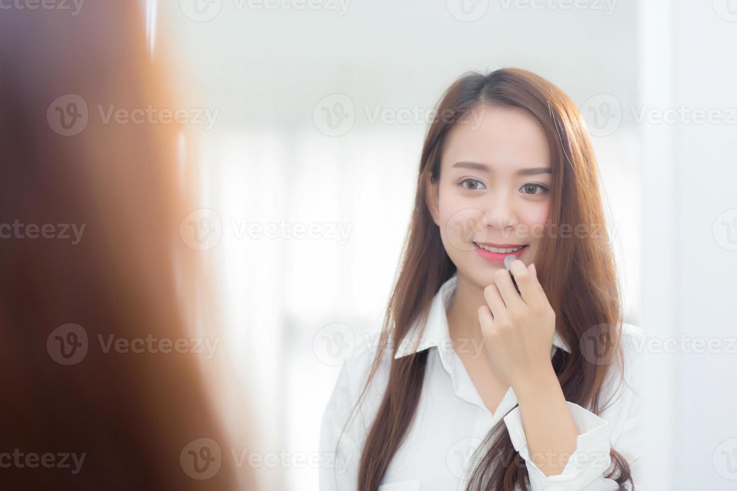 schoonheid van portret van jonge aziatische vrouw aan de spiegel die een make-uplippenstift vasthoudt en kijkt, mooi meisje schoonheidsmode op de kamer, lifestyle concept. foto