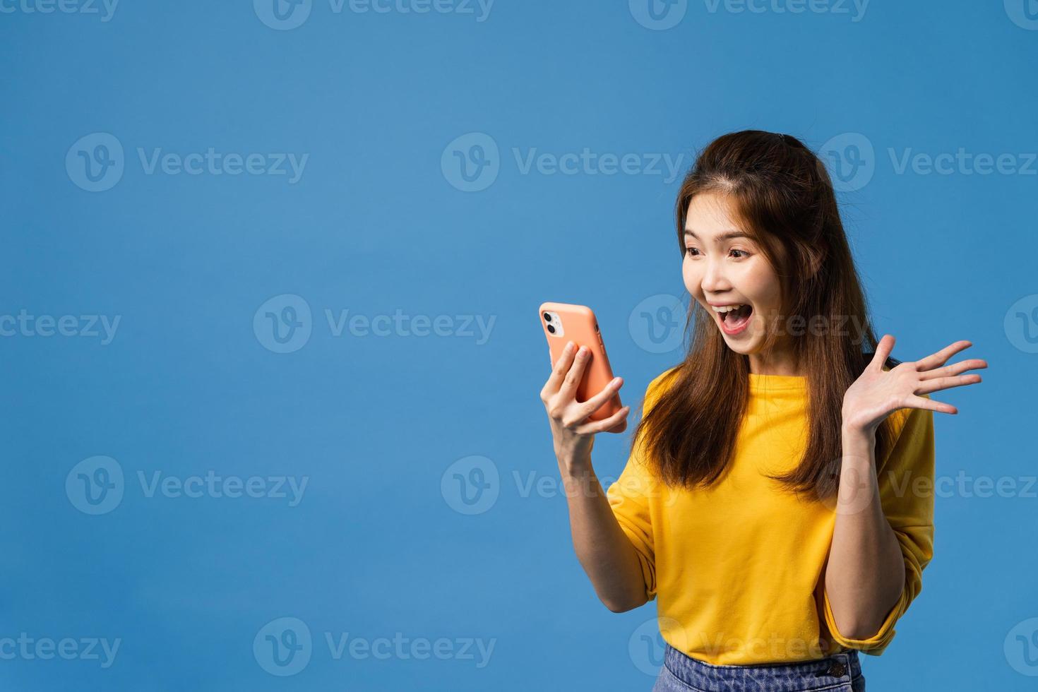 Aziatische dame met behulp van mobiele telefoon positieve uitdrukking op blauwe achtergrond. foto