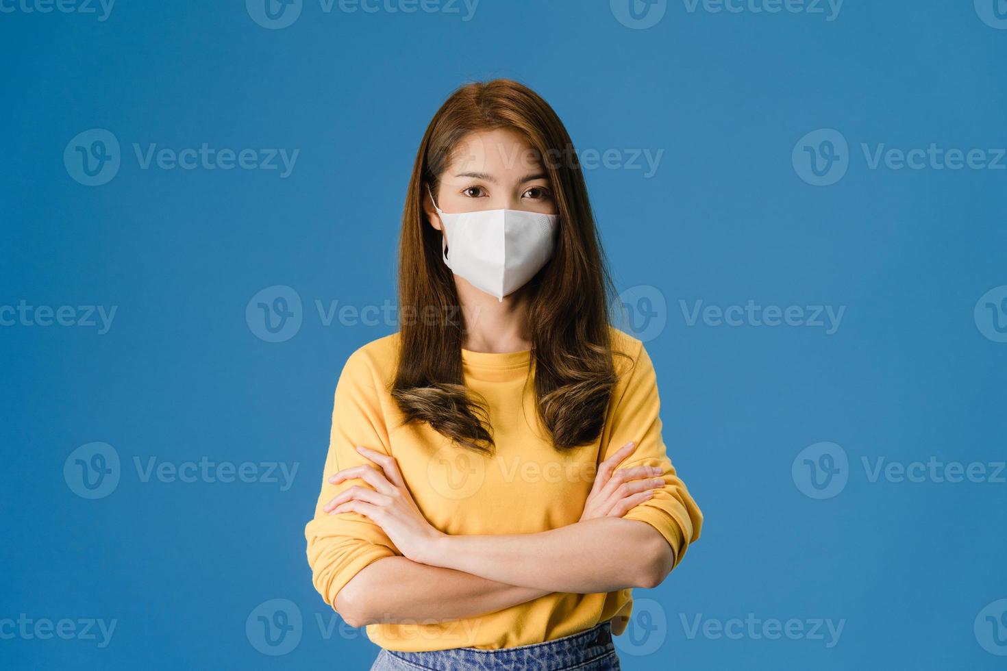 jong Aziatisch meisje draagt een gezichtsmasker met gekruiste armen op een blauwe achtergrond. foto