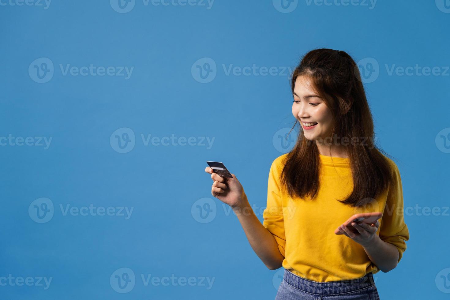 jonge aziatische dame die telefoon en creditcard op blauwe achtergrond gebruikt. foto