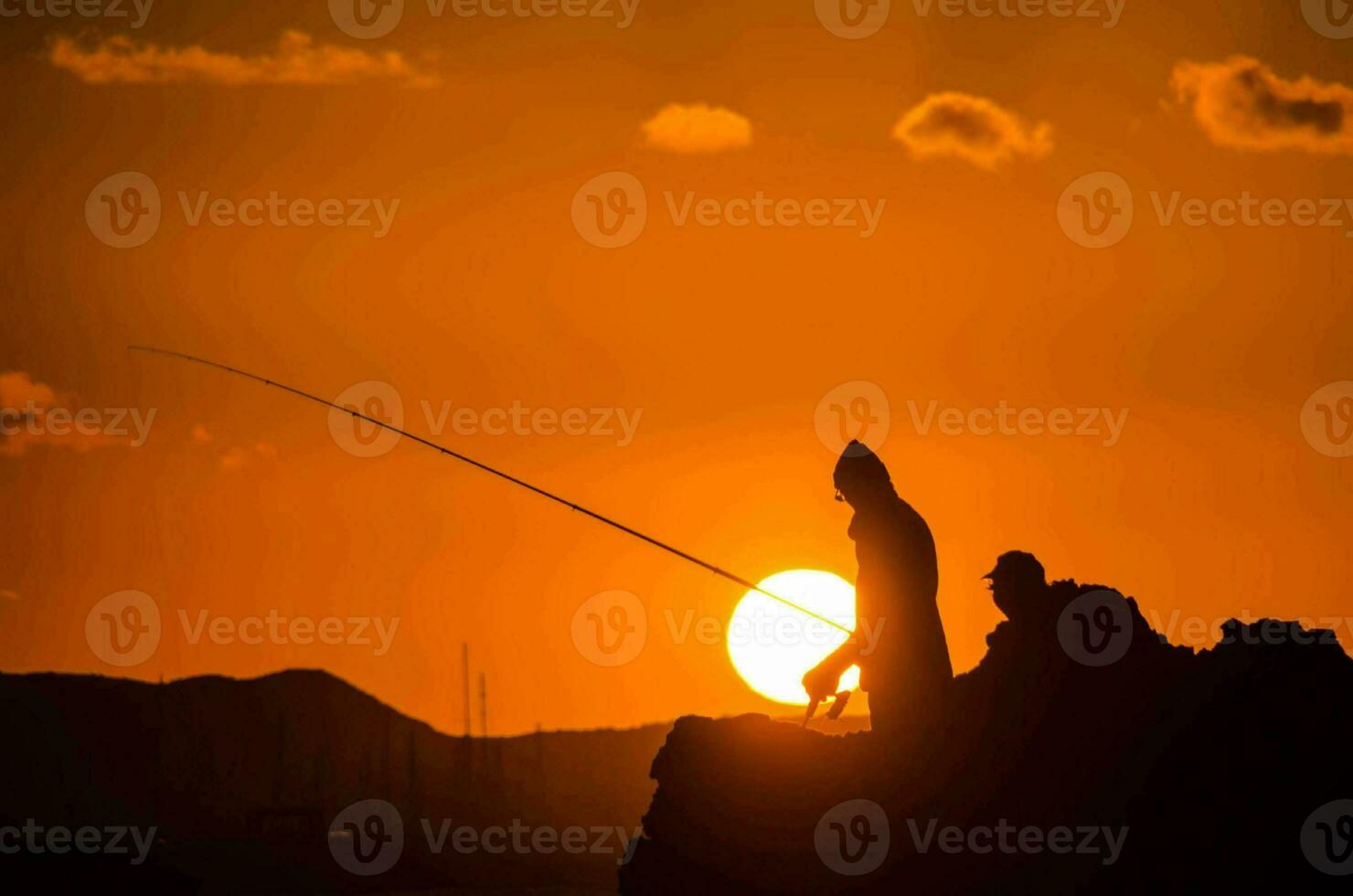 twee mensen visvangst Bij zonsondergang Aan een rots foto