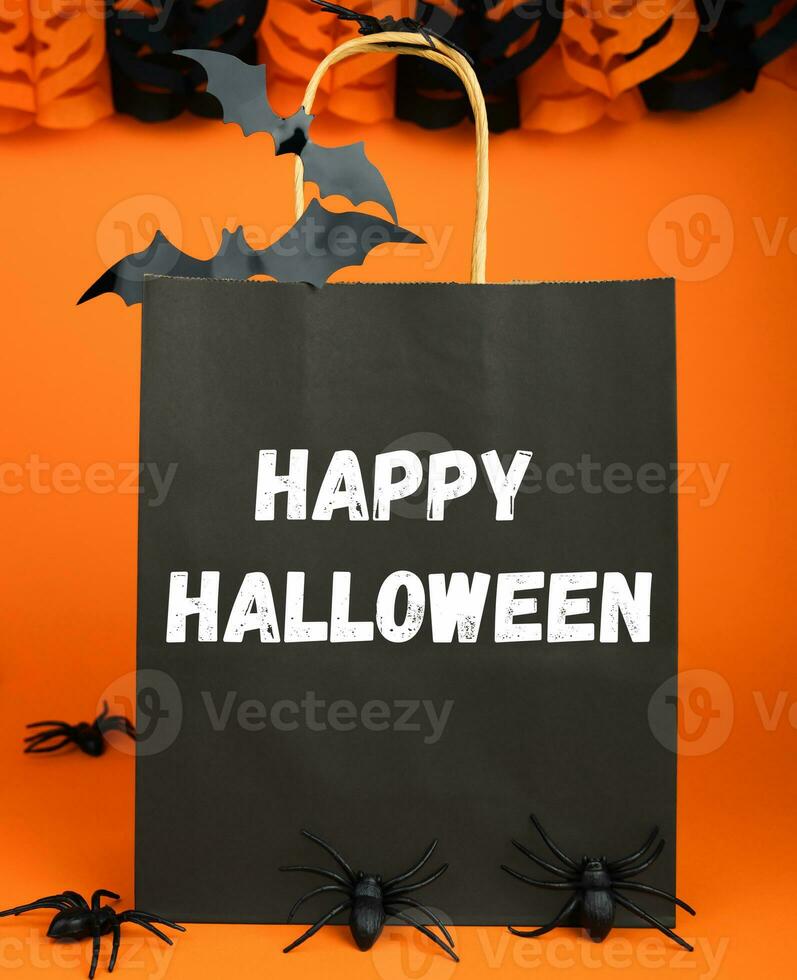 gelukkig halloween. cadeaus en boodschappen doen voor halloween. vakantie kortingen. papier zwart zak en decor voor halloween Aan oranje achtergrond. selectief focus. foto