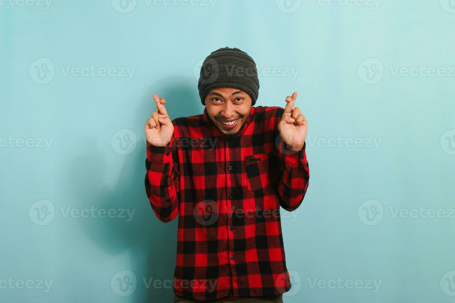 opgewonden jong Aziatisch Mens maakt vinger gekruiste gebaar, geïsoleerd Aan blauw achtergrond foto