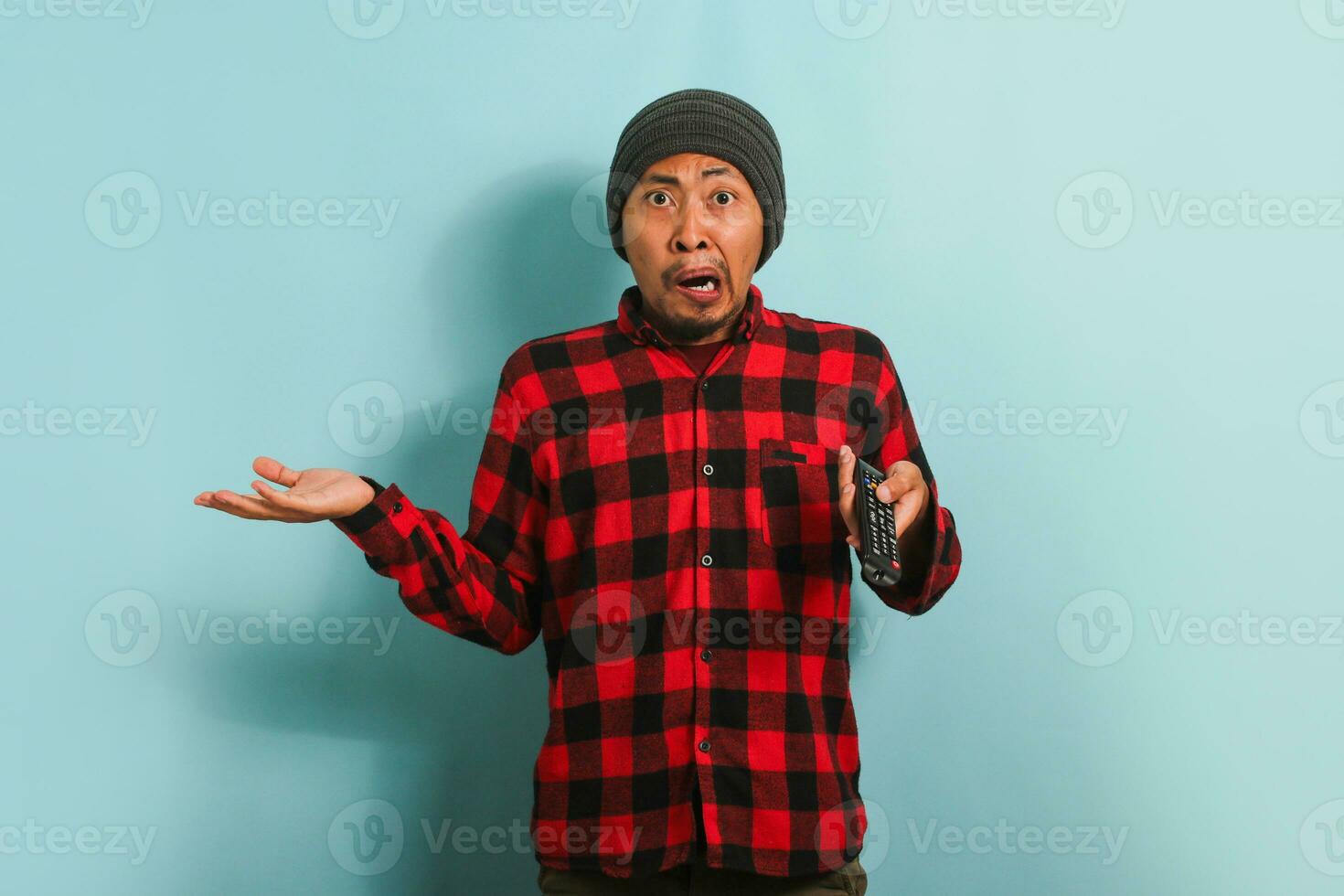 verrast jong Aziatisch Mens aan het kijken schokkend nieuws Aan TV, geïsoleerd Aan een blauw achtergrond foto