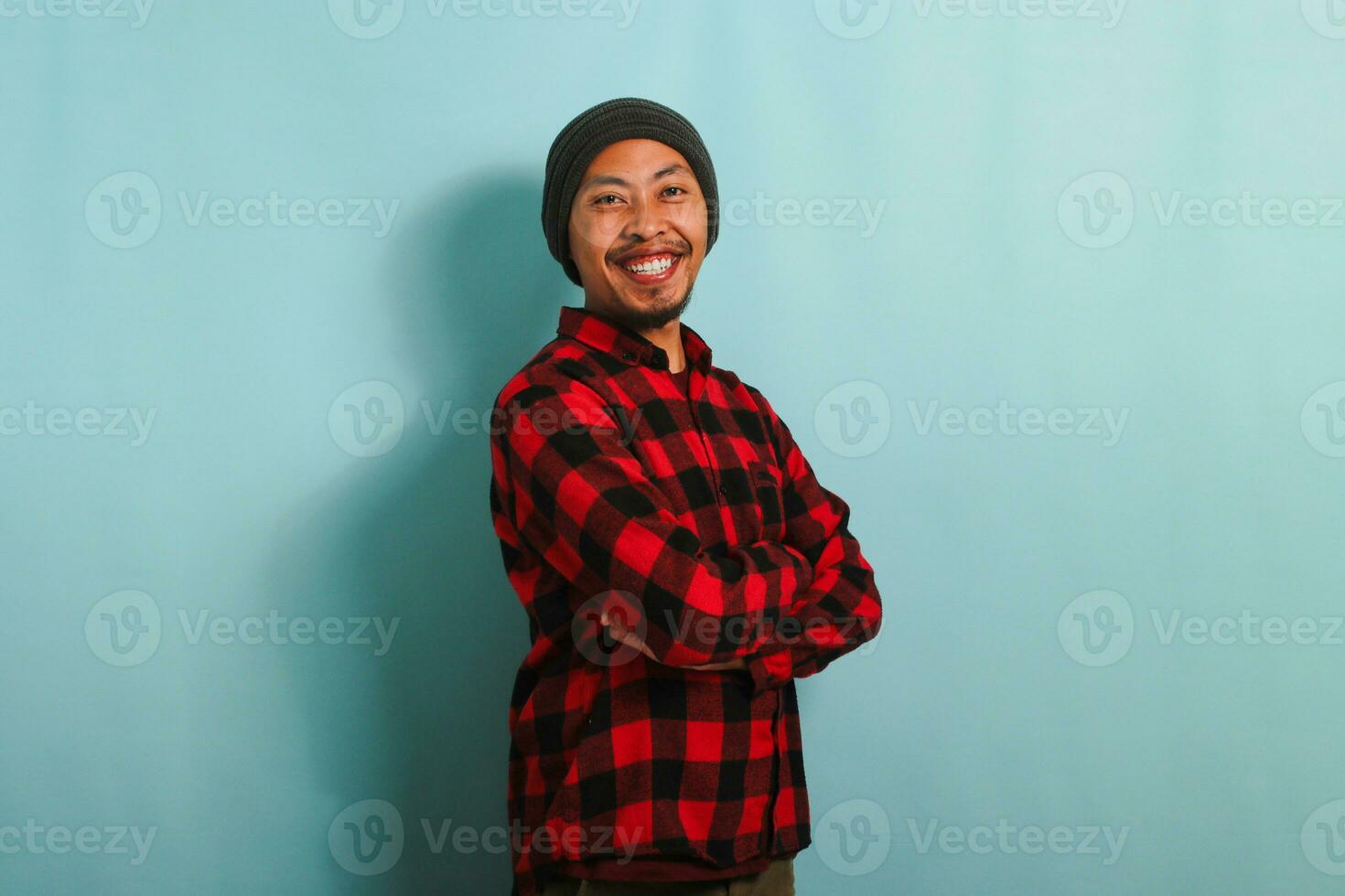 zelfverzekerd jong Aziatisch Mens is op zoek Bij de camera met zijn armen gekruiste geïsoleerd Aan blauw achtergrond foto