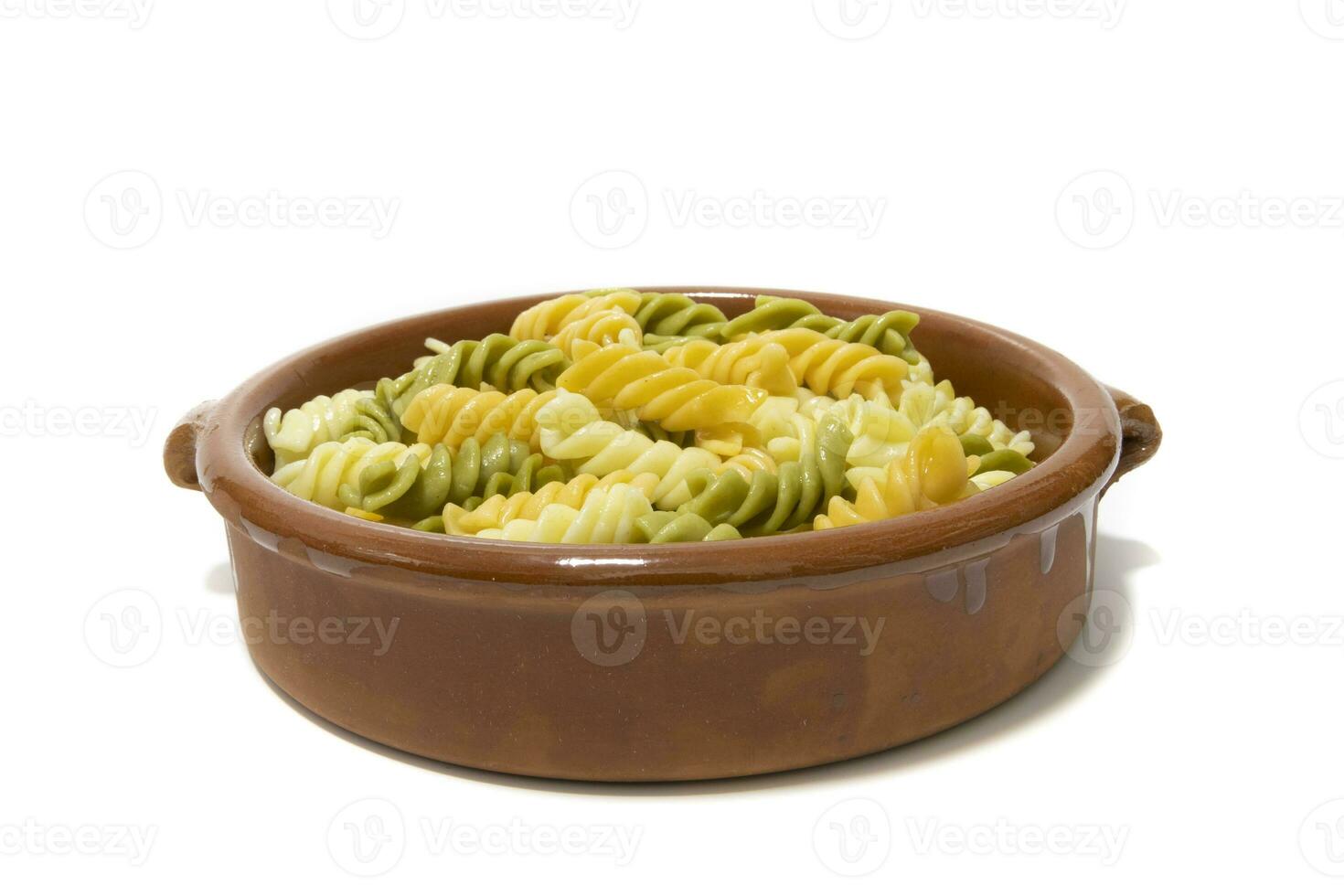 spiraal pasta van drie kleuren, geserveerd in een klei schaal. geïsoleerd Aan een wit achtergrond. vegetarisch voedsel concept. foto