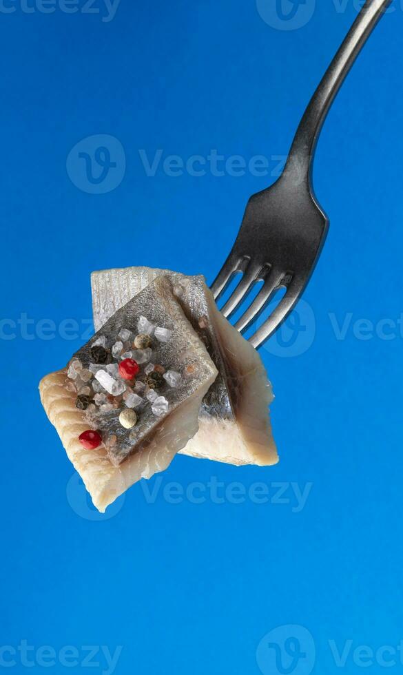 stukken van gezouten haring Aan vork geïsoleerd Aan blauw achtergrond foto