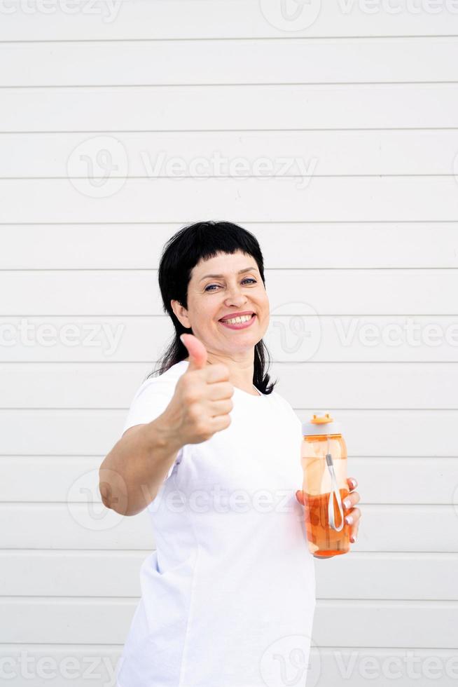 vrouw die water drinkt en duimen op een achtergrond laat zien foto
