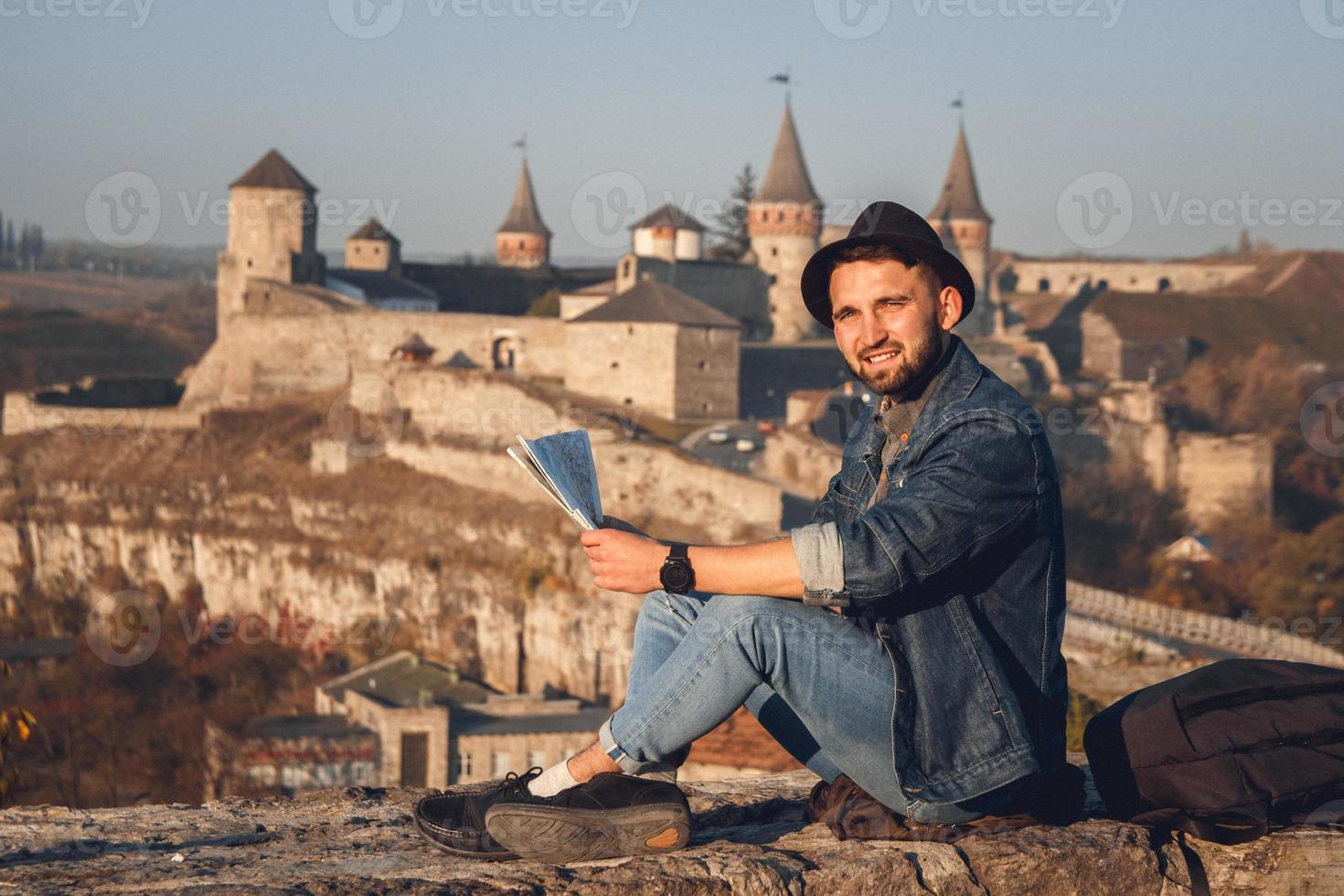 reiziger man met een kaart in zijn handen zit op de achtergrond van het oude kasteel foto