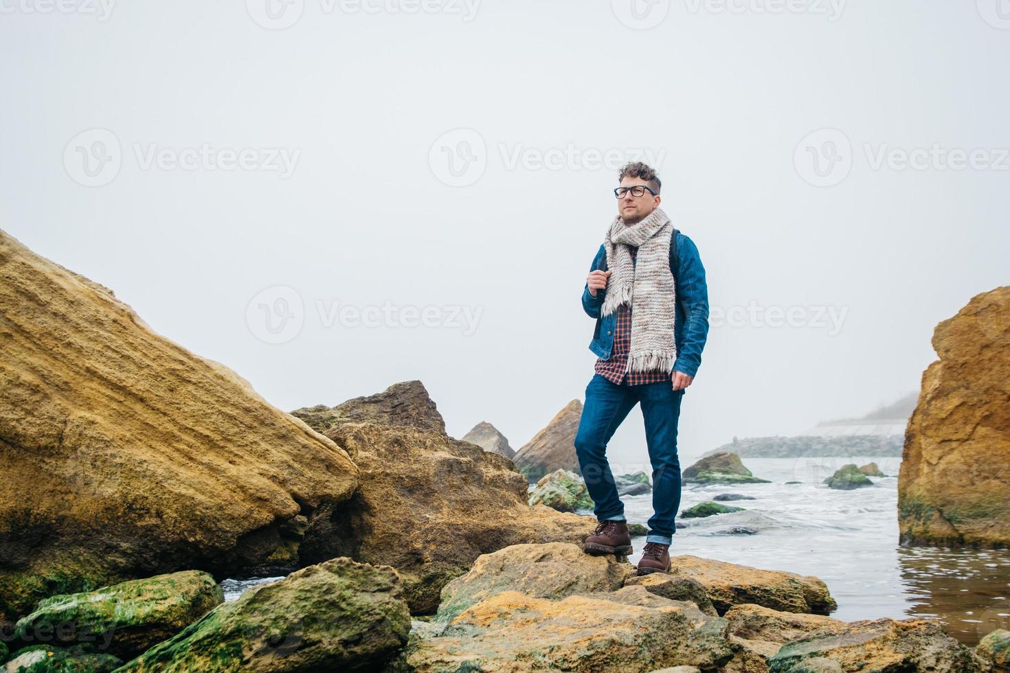 man met een rugzak die op een rots staat tegen een prachtige zee foto