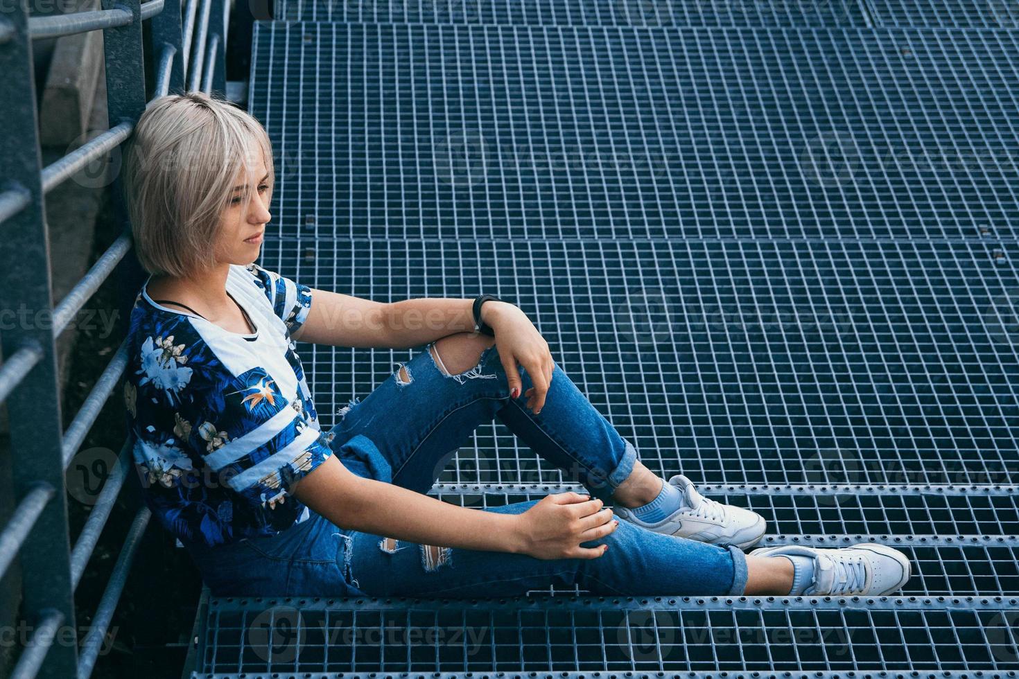 vrouw met kort wit haar in stedelijke stijl zit op de metalen trap foto