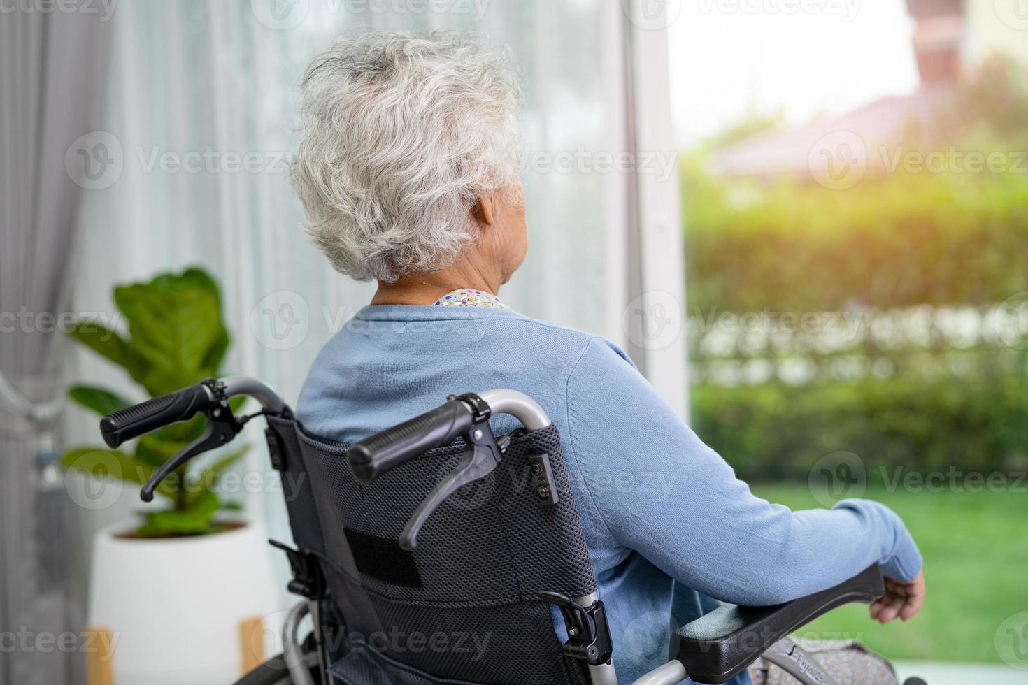 oudere vrouw die in een rolstoel zit en uit het raam kijkt foto