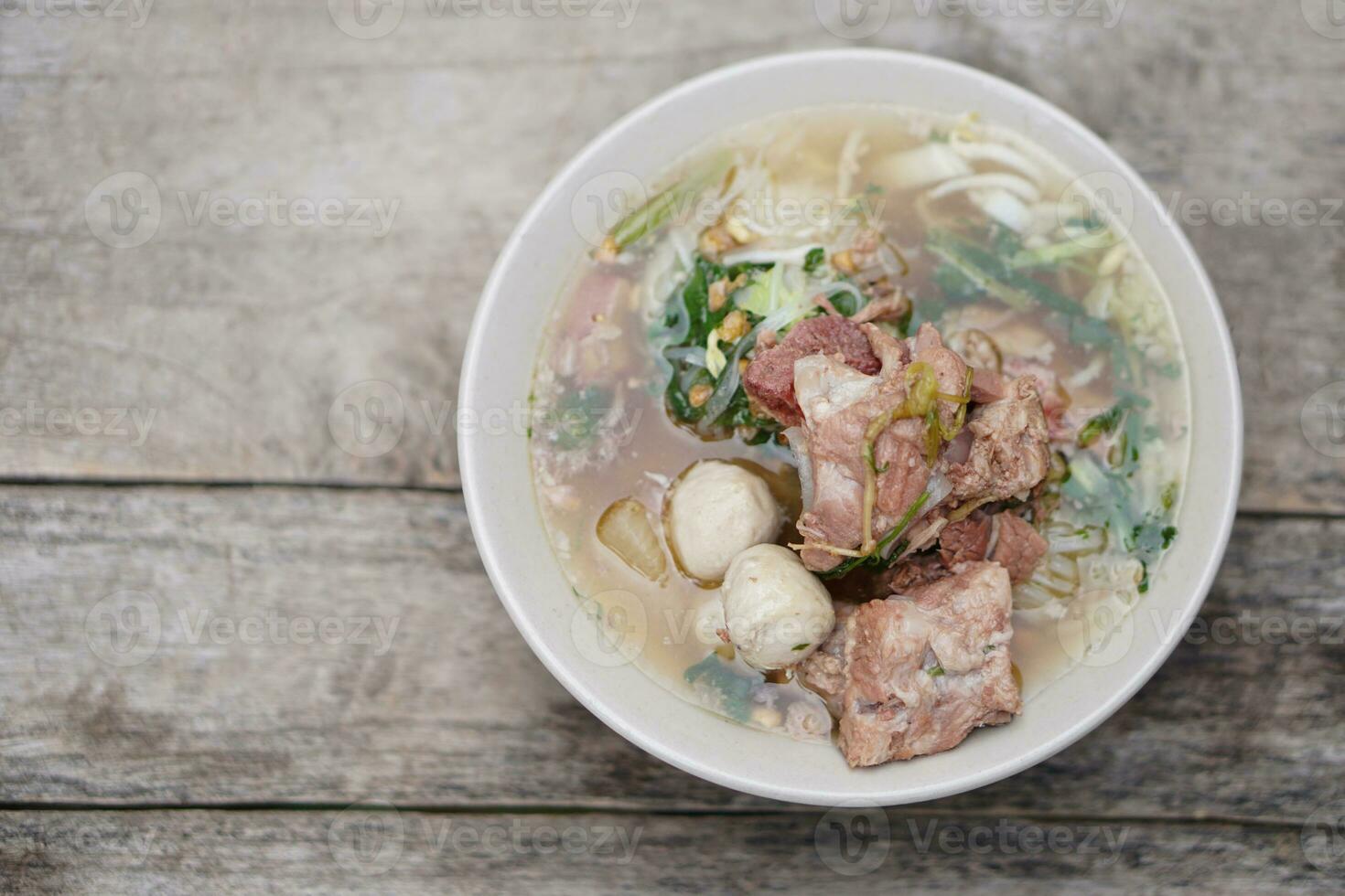 gestoofd varkensvlees soep met vlees ballen en groenten in schaal, oud houten achtergrond. concept, traditioneel voedsel. favoriete menu dat kan koken of bestellen in noodle levensmiddelenwinkels in Thailand. foto