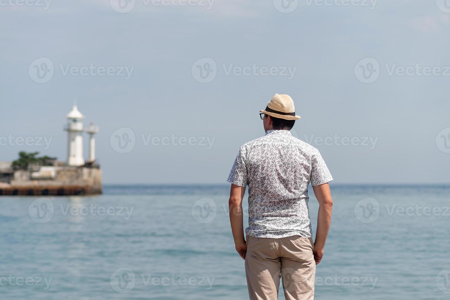 man die op de pier staat met de zee en de vuurtoren op de achtergrond foto