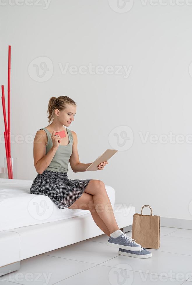 jonge vrouw die online winkelt om thuis op bed te zitten foto