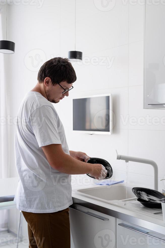 man in wit t-shirt afwassen in de keuken foto