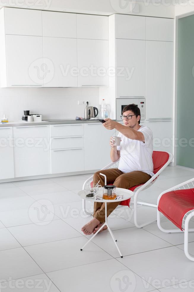 man zit in een stoel tv te kijken met afstandsbediening foto