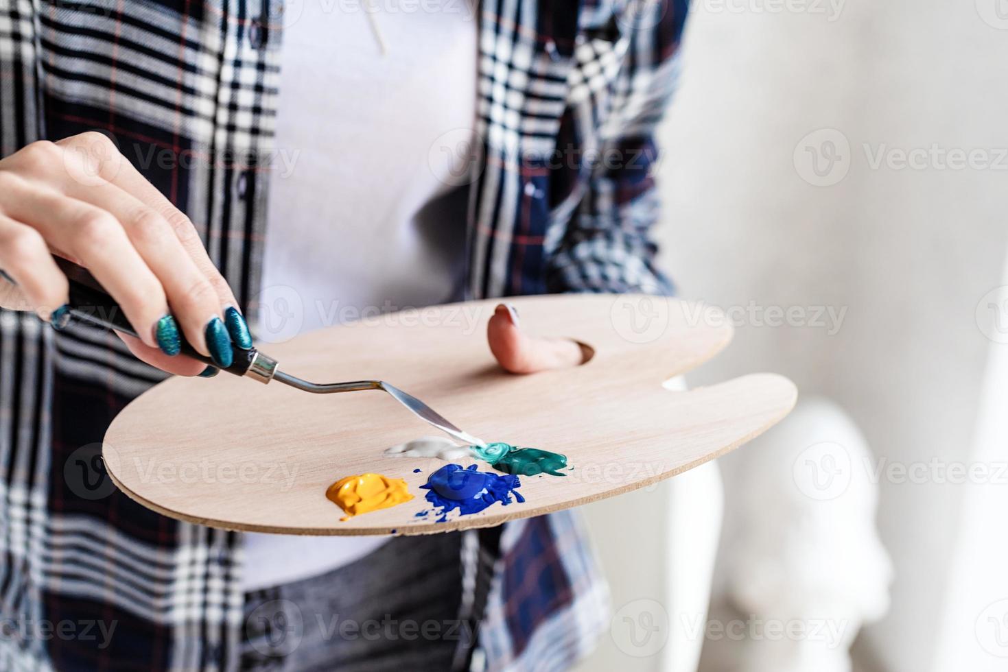 close-up van vrouwelijke kunstenaarshanden die kleuren mengen op houten kunstpalet foto