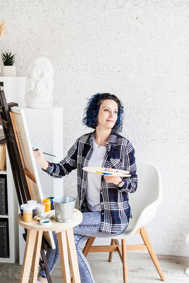 creatieve vrouw met blauw geverfd haar schilderij in haar atelier foto