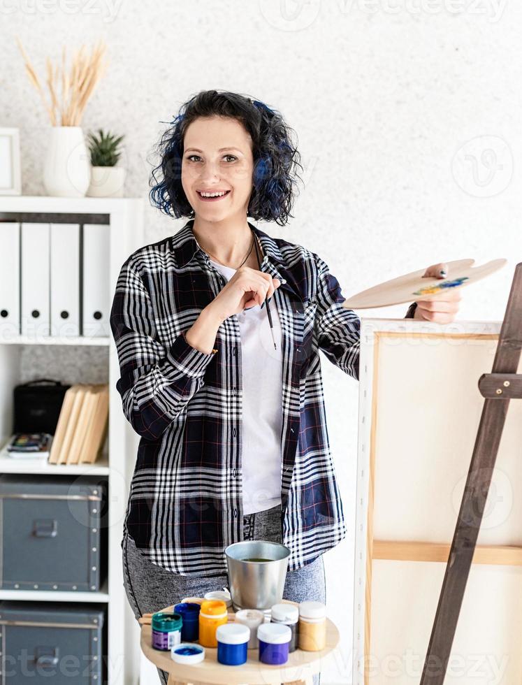 creatieve vrouw met blauw geverfd haar schilderij in haar atelier foto