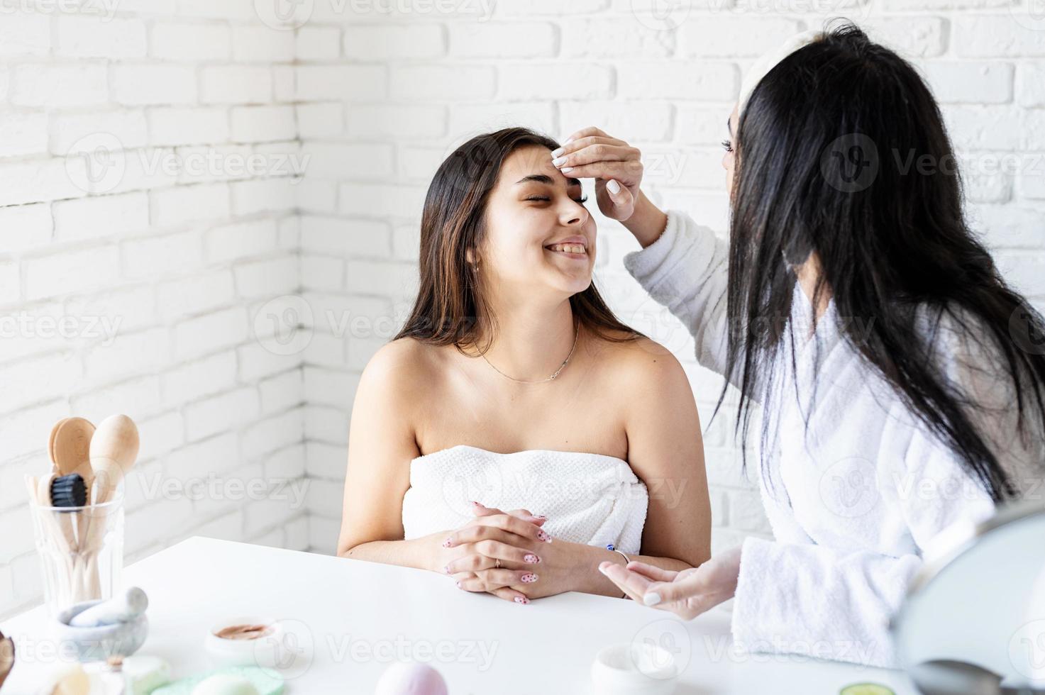 twee mooie vrouwen die gezichtscrème aanbrengen die spa-procedures doen foto