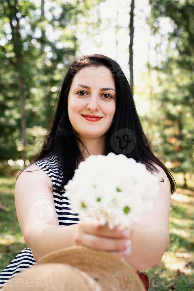 volwassen brunette vrouw van middelbare leeftijd die buiten staat en verse bloemen ruikt foto