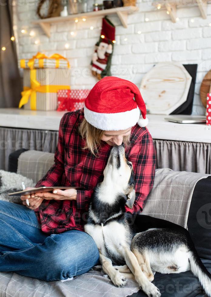 vrouw in kerstmuts die op tablet werkt terwijl ze met haar hond op de bank zit foto