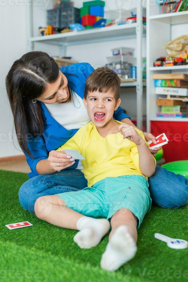 schattig vrouw toespraak therapeut geeft les kind naar uitspreken woorden geluiden en brieven correct in kantoor foto