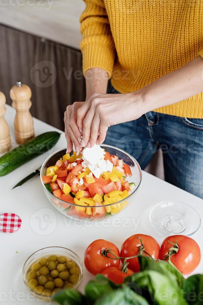 vrouwelijke handen maken salade snijden fetakaas in de keuken foto