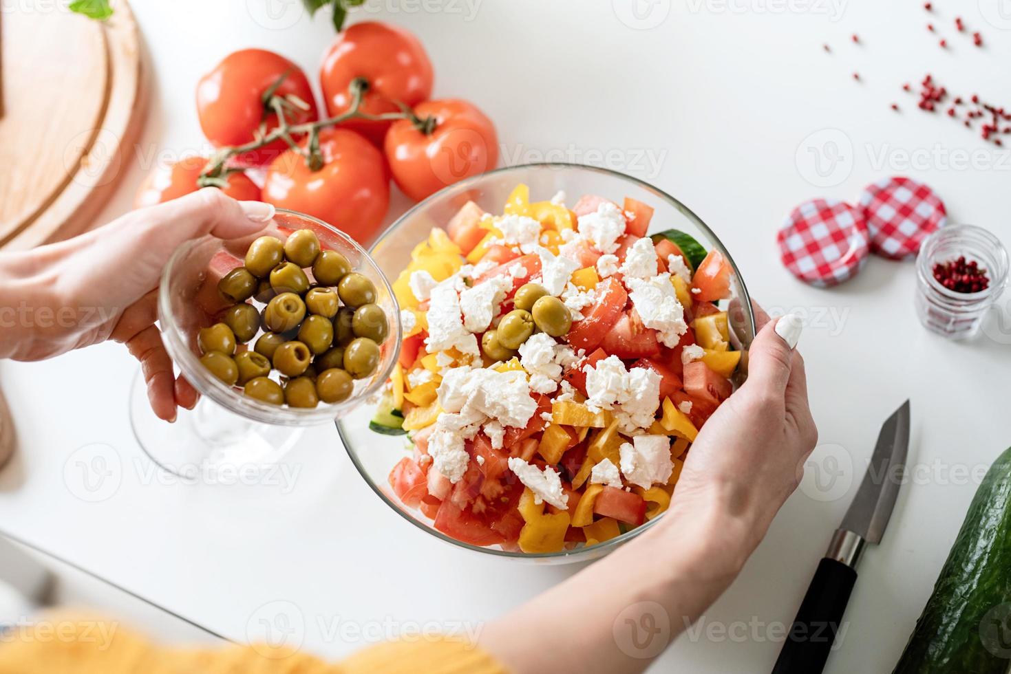 vrouwelijke handen die Griekse salade maken die olijven aan de kom toevoegen foto