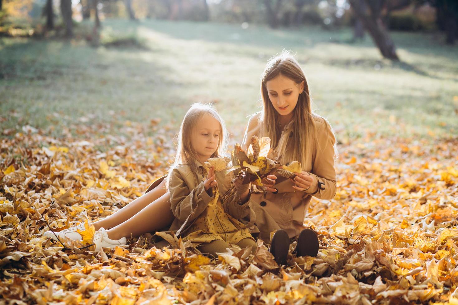 moeder en haar dochter zitten en hebben plezier in het herfstpark. foto