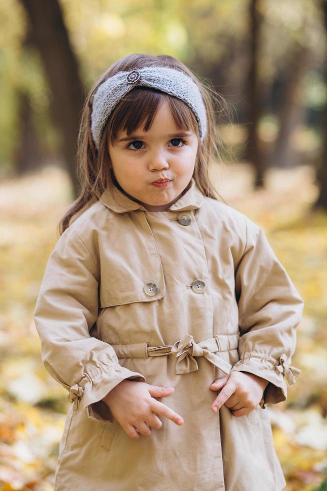 gelukkig klein meisje in een beige jas loopt in het herfstpark foto