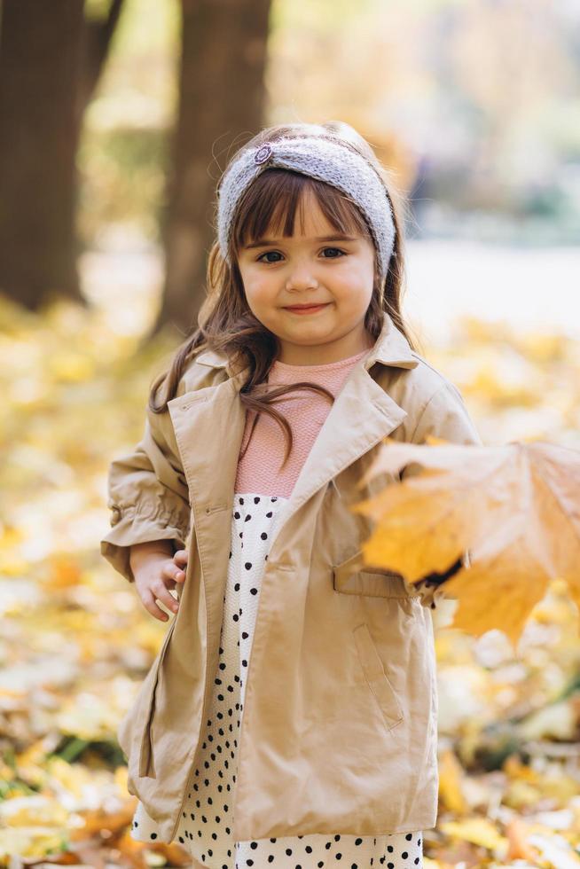 mooi klein meisje met een geel esdoornblad in het herfstpark foto
