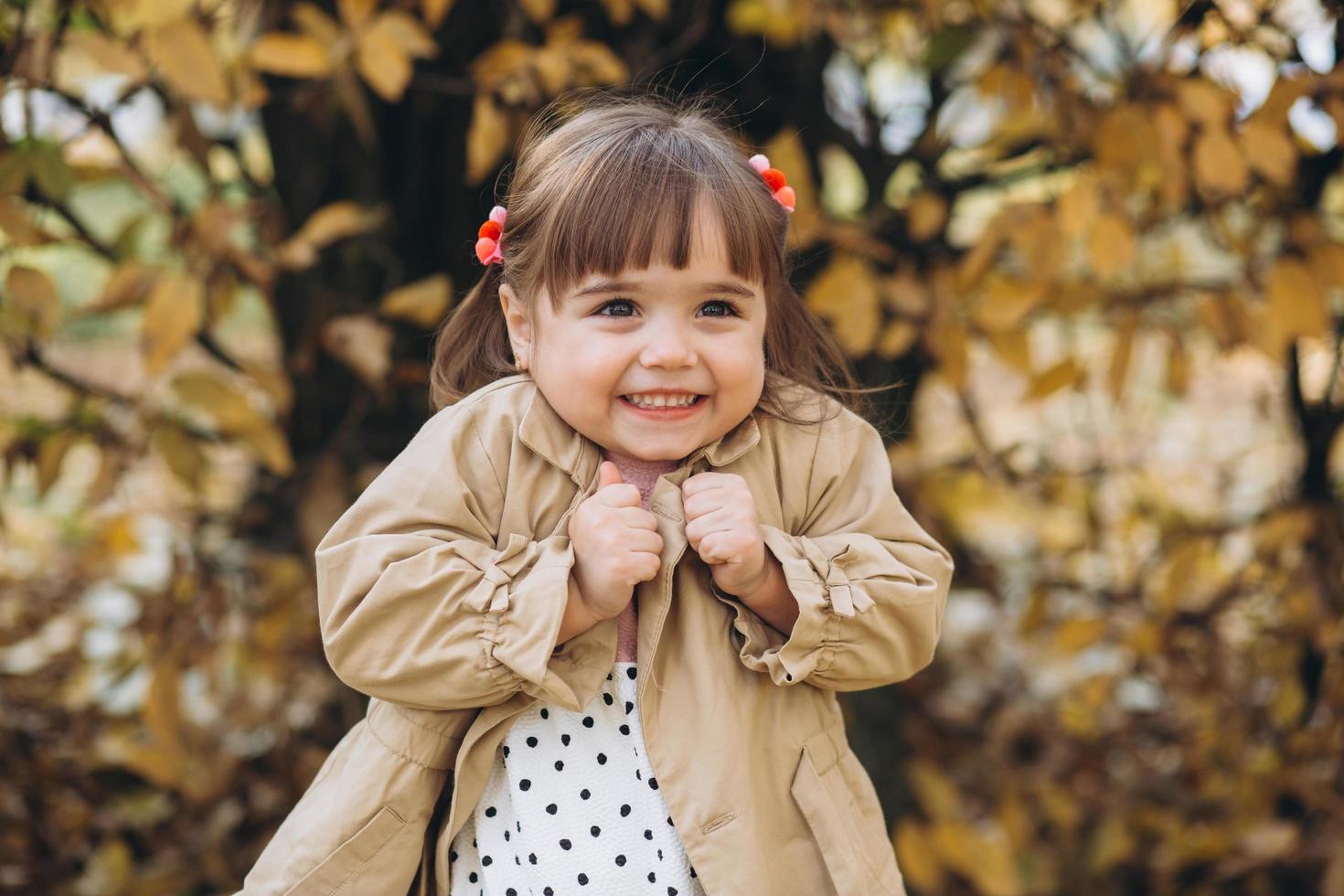 klein meisje in een beige jas toont emoties in het herfstpark foto
