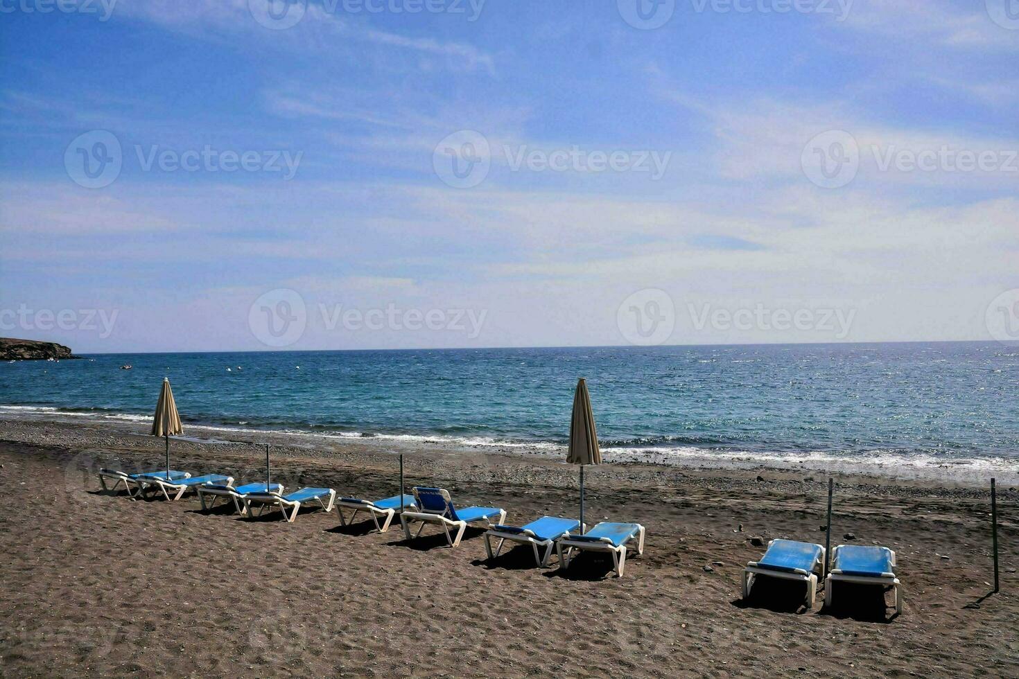 een strand met lounge stoelen en paraplu's Aan het foto