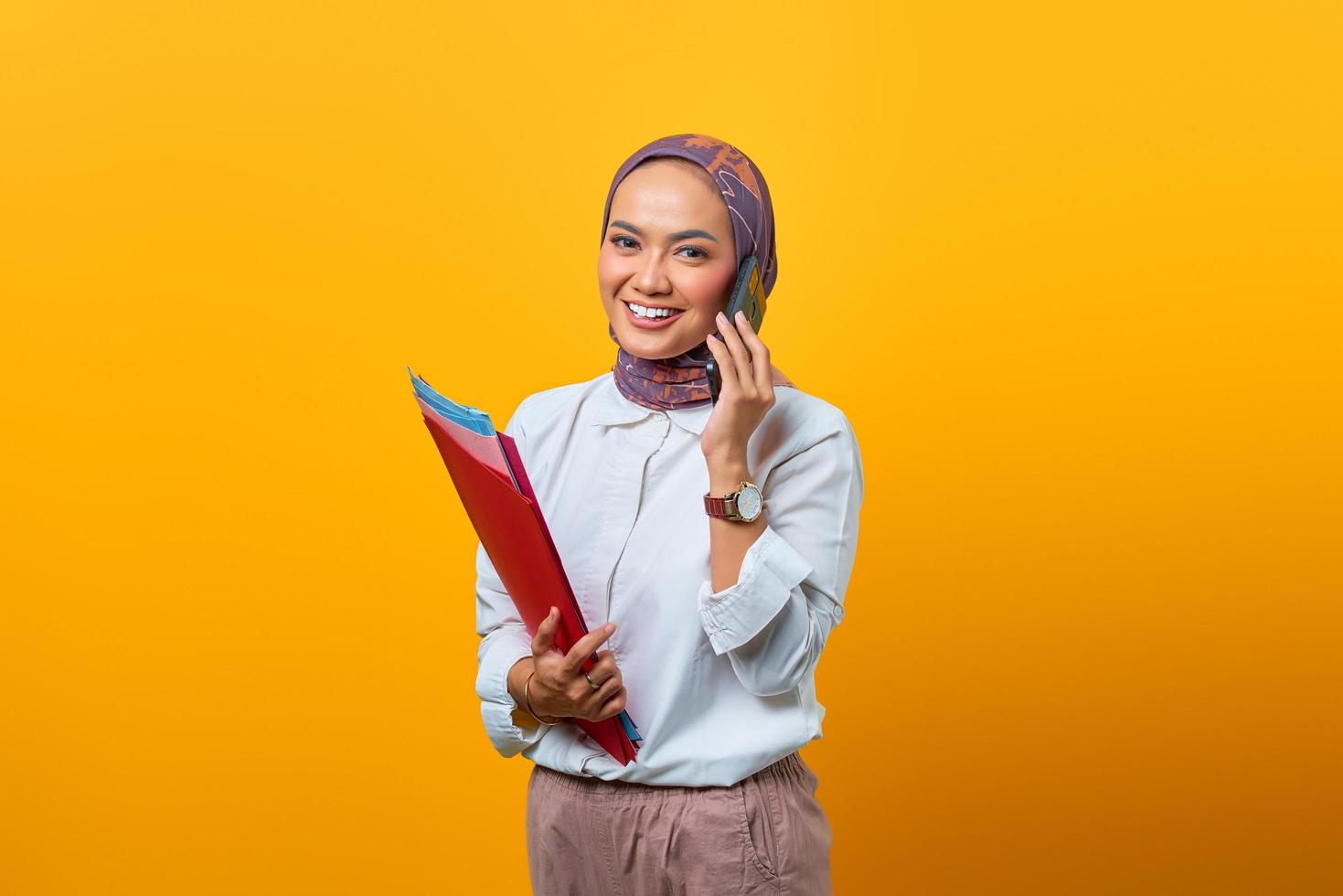 mooie aziatische vrouw die mappen vasthoudt en op mobiele telefoon praat foto