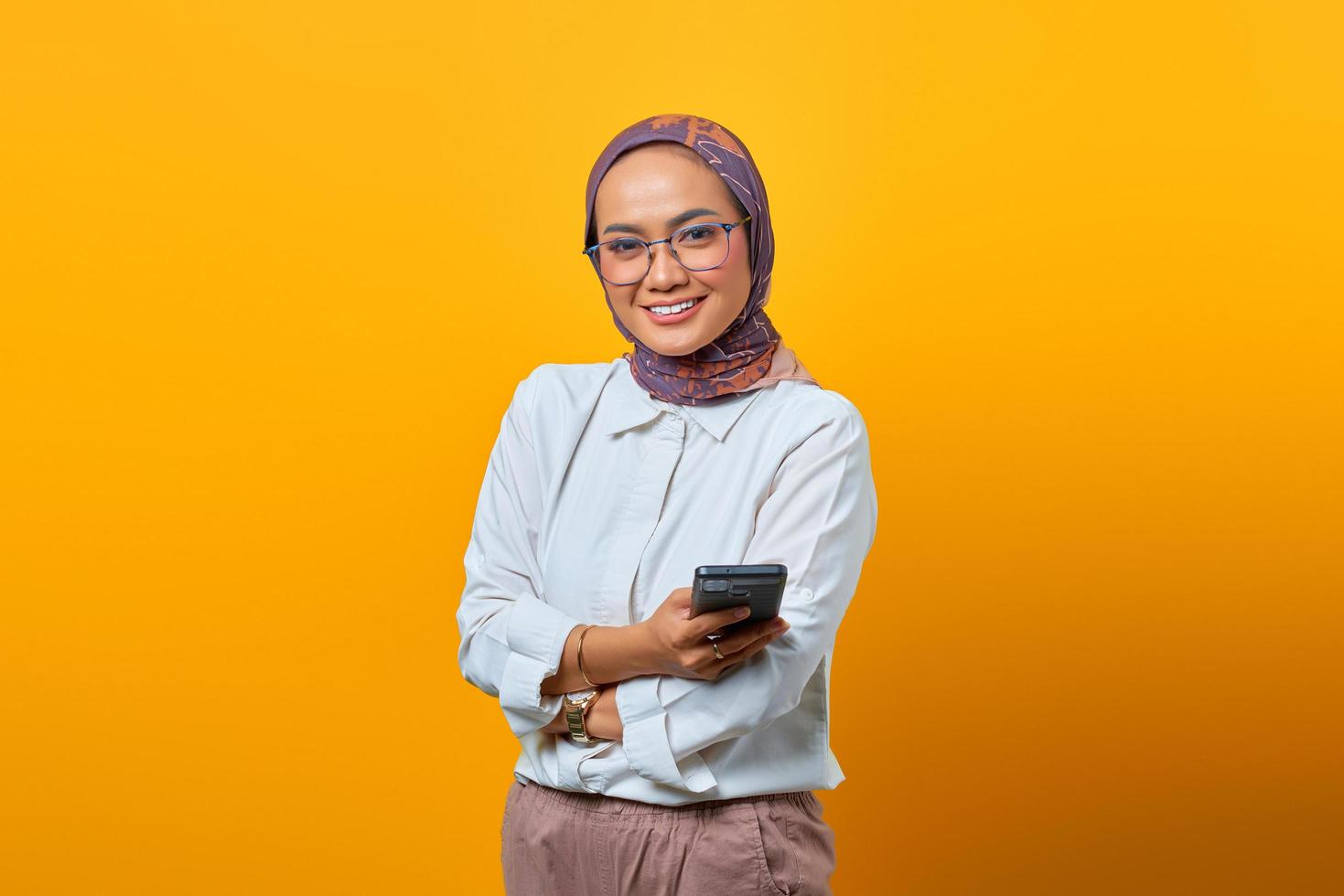 lachende aziatische vrouw met mobiele telefoon met gekruiste armen foto