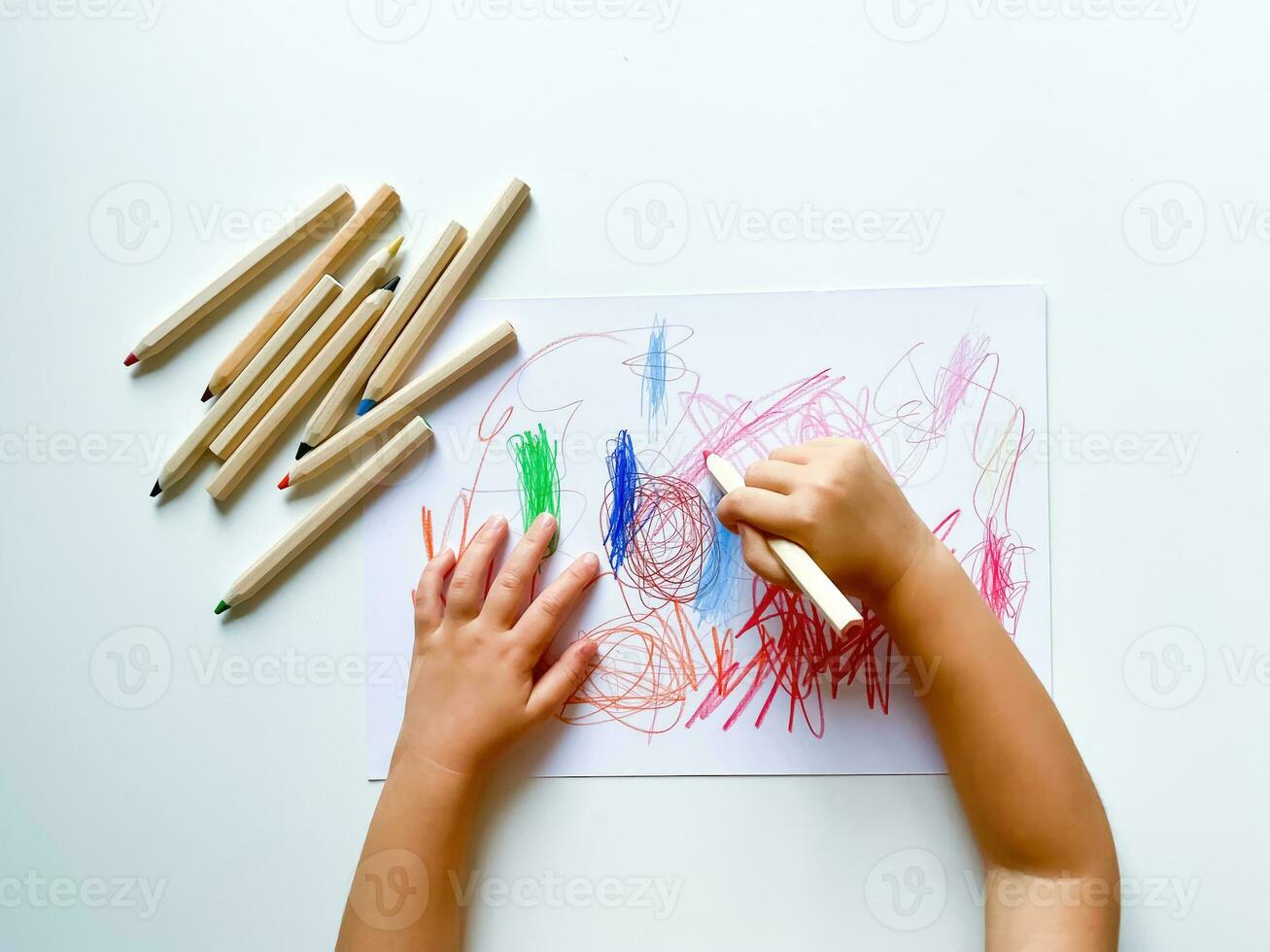 klein kind trekt met gekleurde potloden Aan papier Aan wit tafel. foto