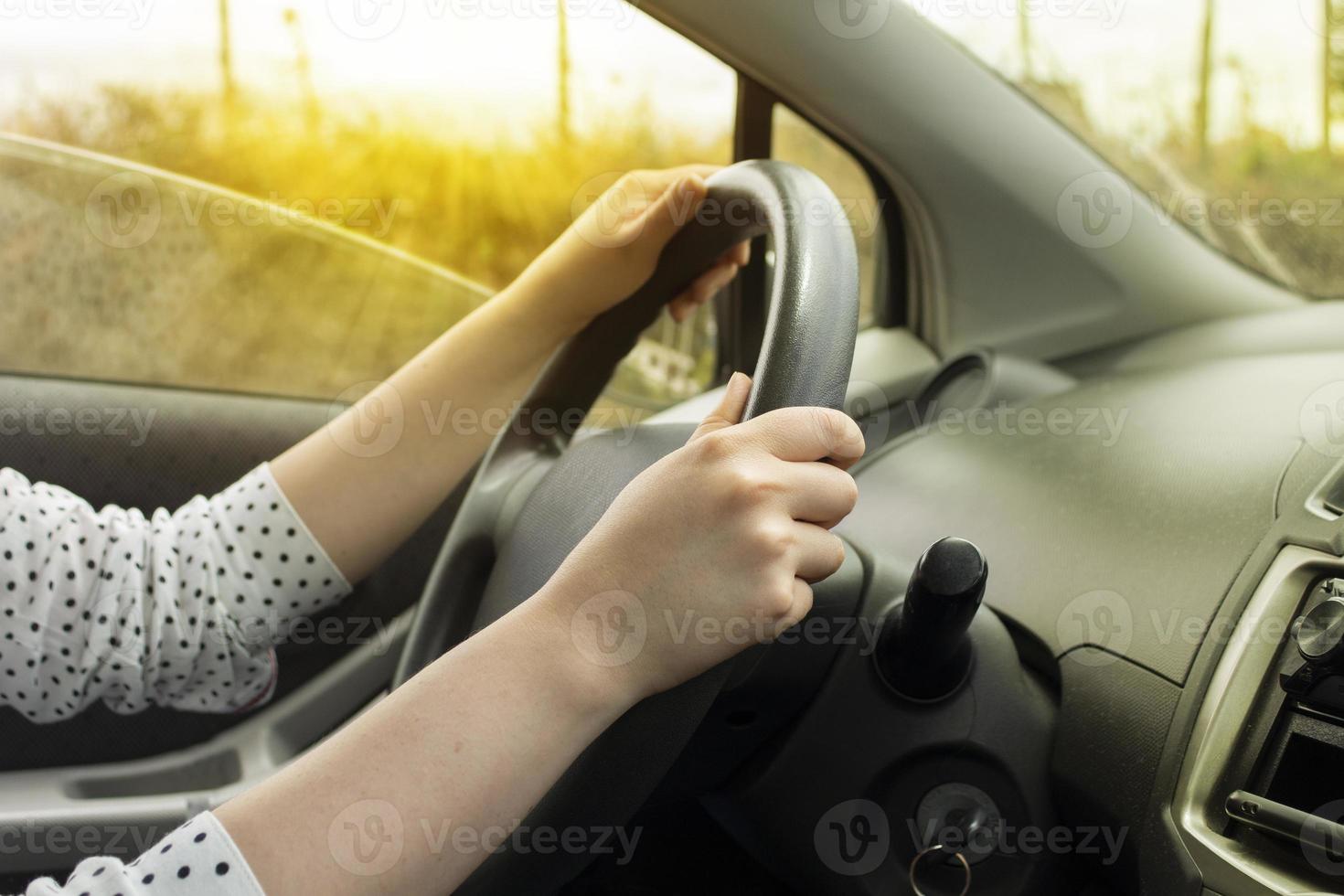 handen van een vrouw aan het stuur van een rijdende auto bij zonsondergang foto