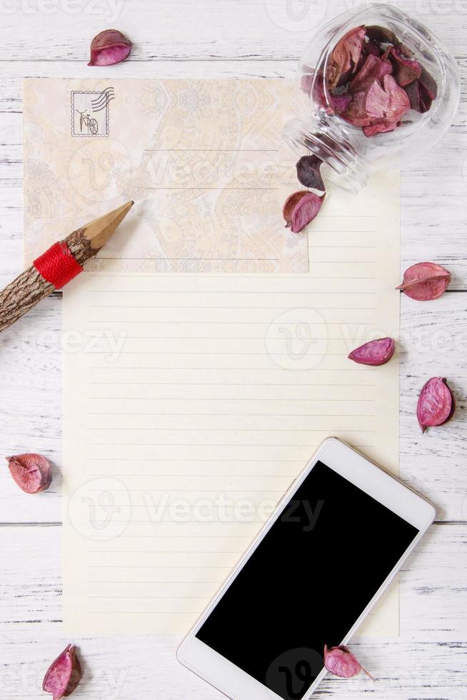 papier met potlood, telefoon en bloemblaadjes foto